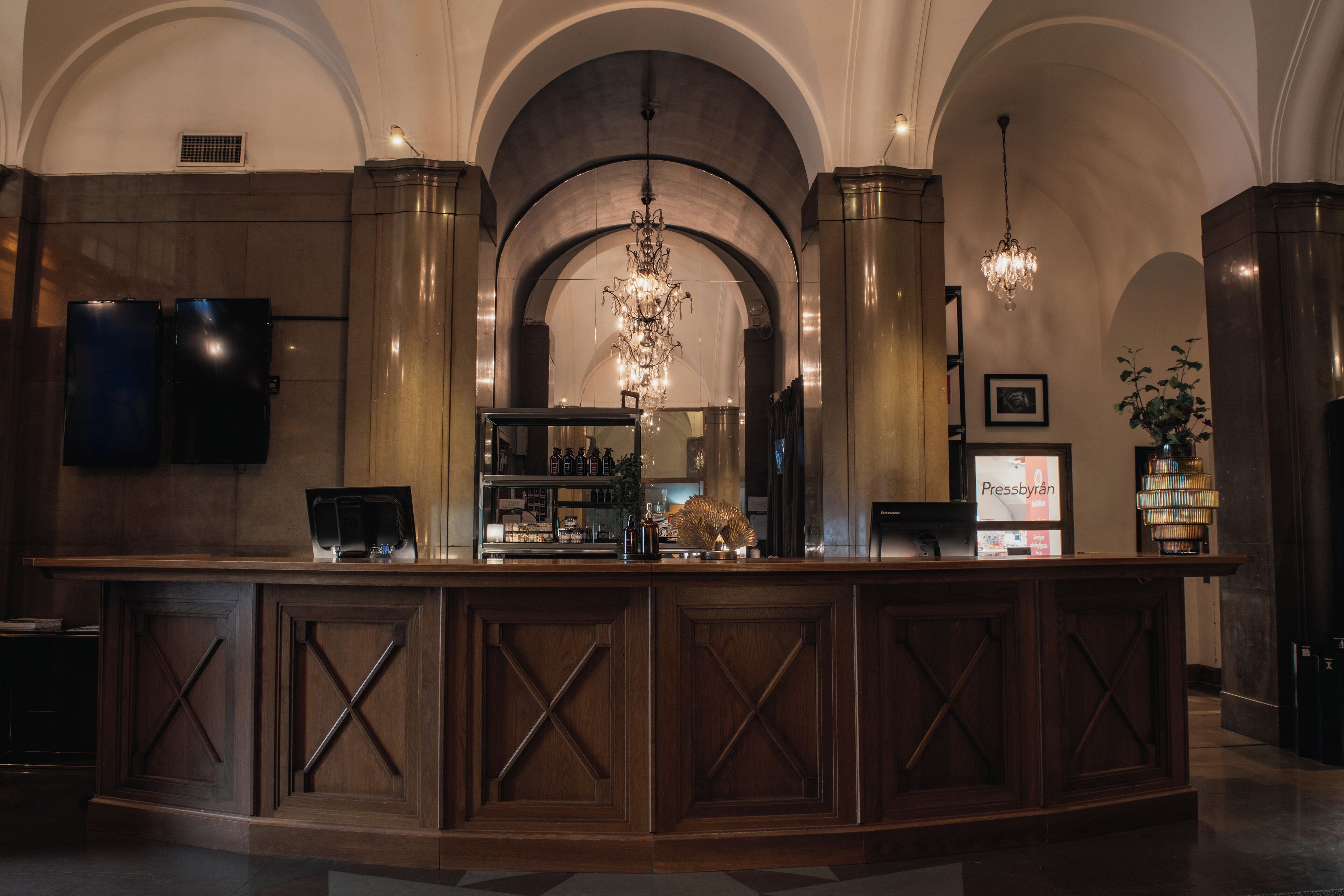 A bar area with a wooden counter, arched ceiling, chandeliers, and a television screen.