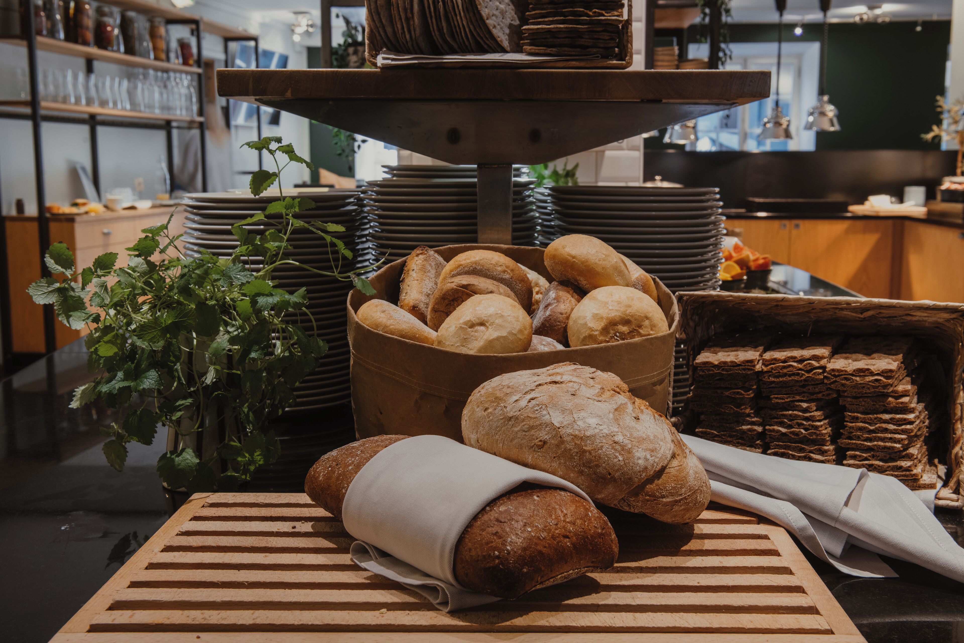 A bakery display with various breads and pastries, a wooden cutting board, and a potted plant.