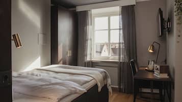Un dormitorio con cama, escritorio, silla, ventana con cortinas y lámpara de pared.