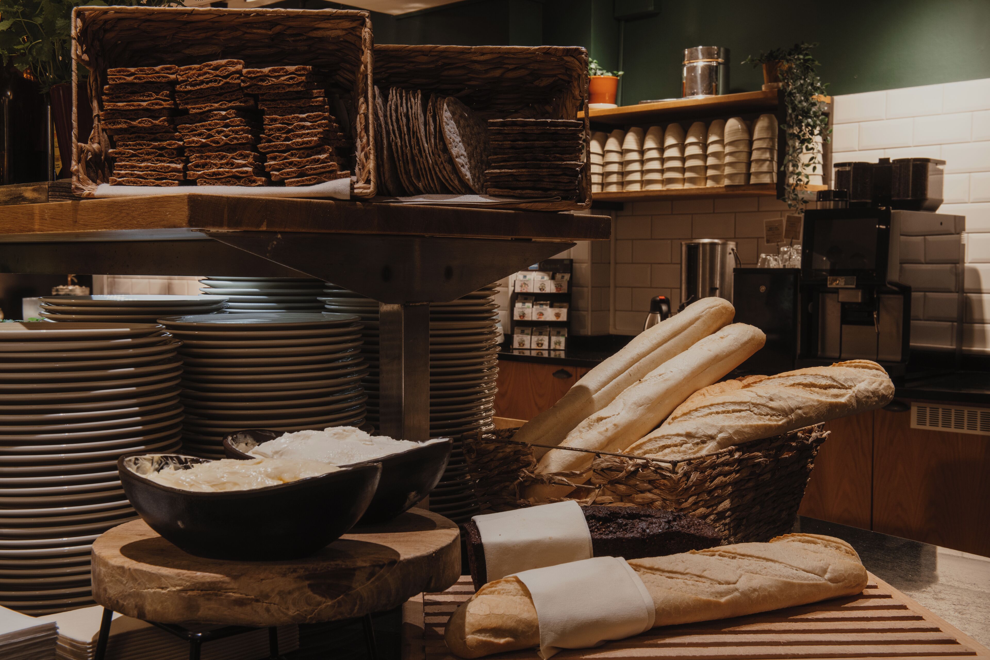 A kitchen with stacks of plates, a bowl of rice, and several loaves of bread.