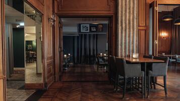 A wooden interior with a herringbone floor, a bar area with bar stools, and a dining area with tables and chairs.