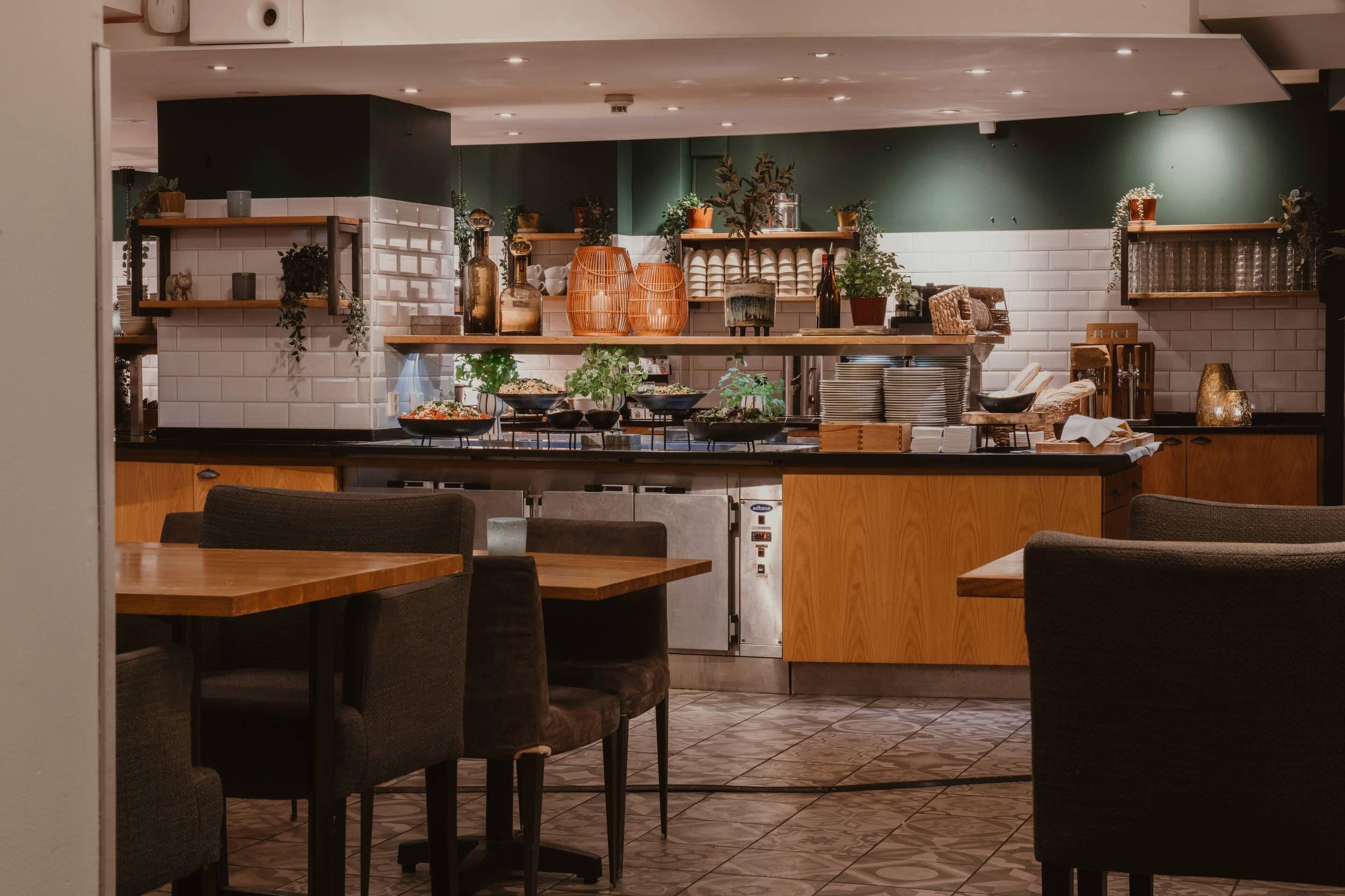 En modern restaurang med en central ö, ett sittområde och dekorativa växter.