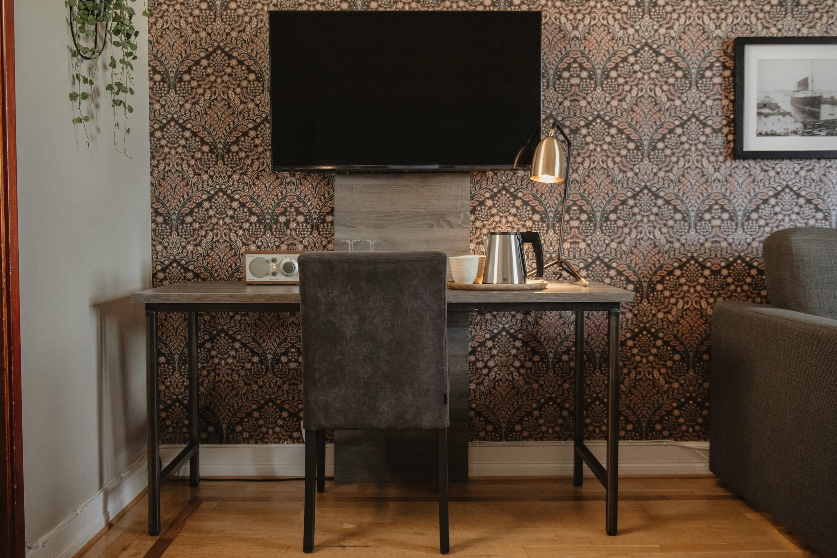 Una sala de estar moderna con una televisión de pantalla plana montada en la pared, una mesa con una silla, una cafetera y un cuadro enmarcado.