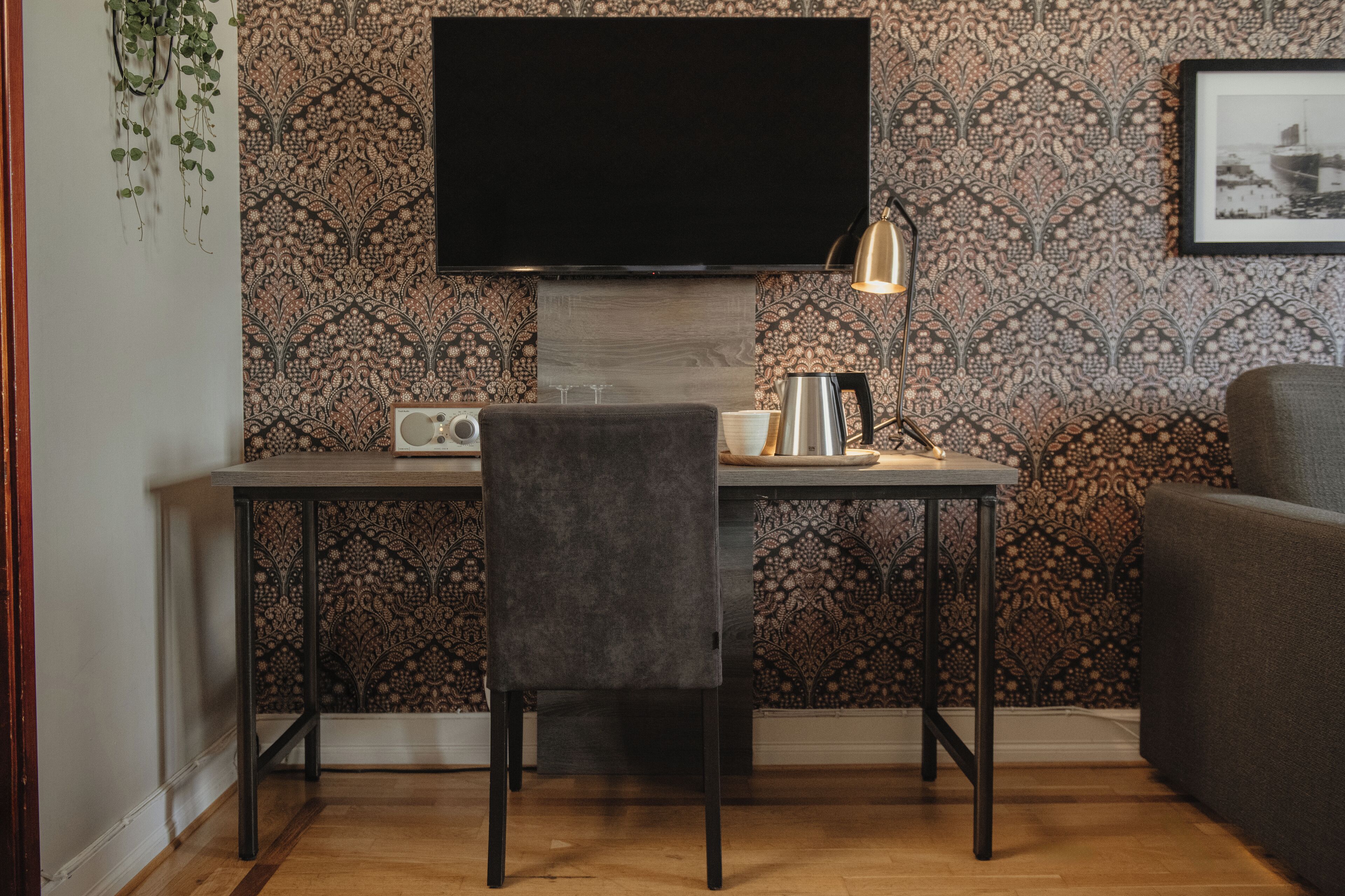 A modern room with a flat-screen TV mounted on the wall, a table with a chair, a lamp, and a framed picture on the wall.