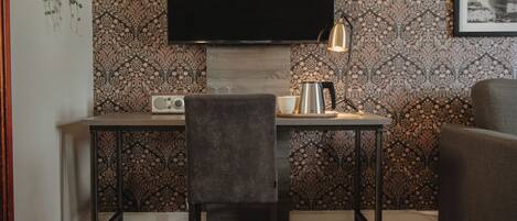 A modern room with a flat-screen TV mounted on the wall, a table with a chair, a lamp, and a framed picture on the wall.