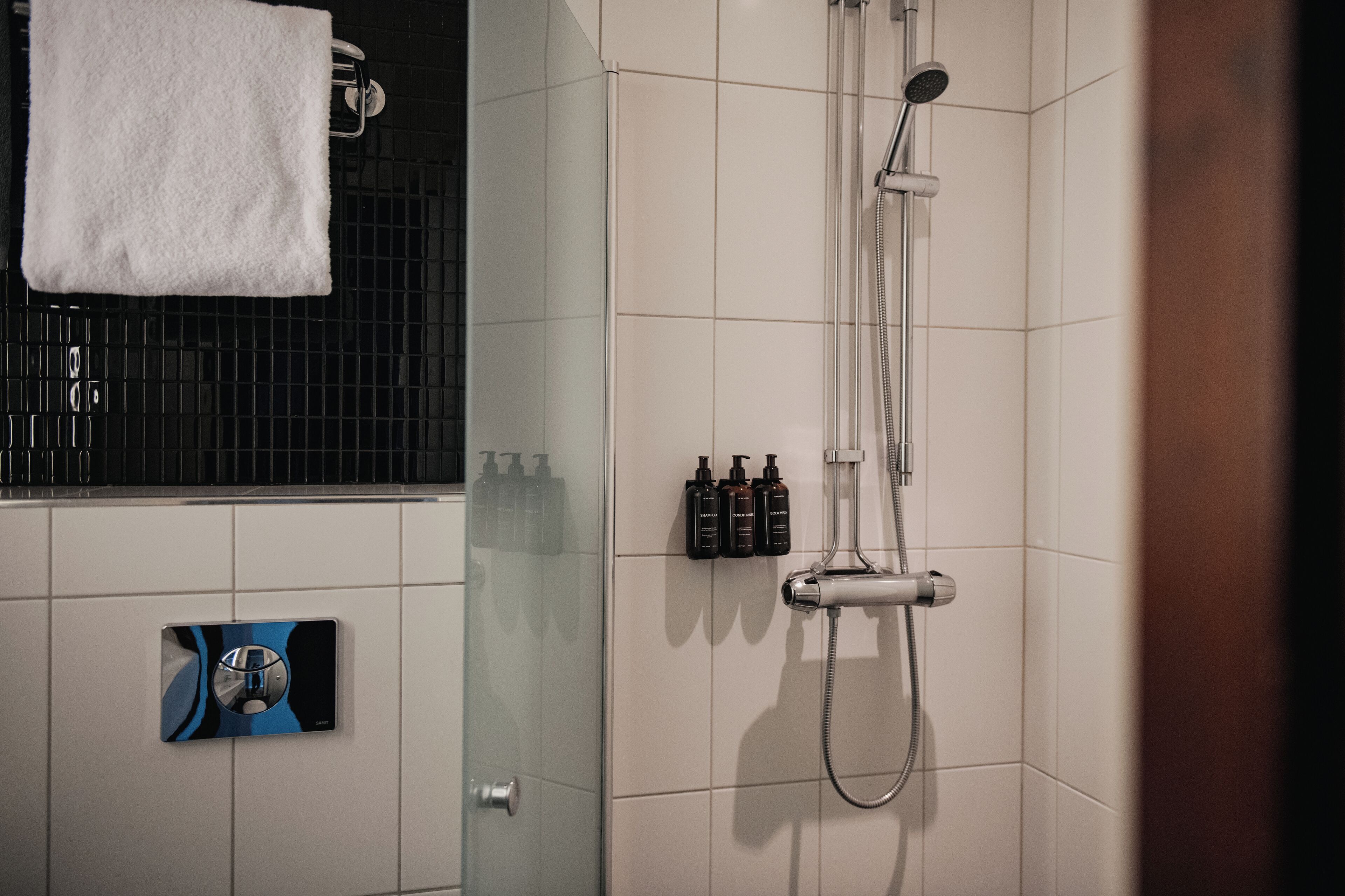 Un baño con cabina de ducha de vidrio, una toalla en un perchero y un juego de artículos de tocador en la pared.