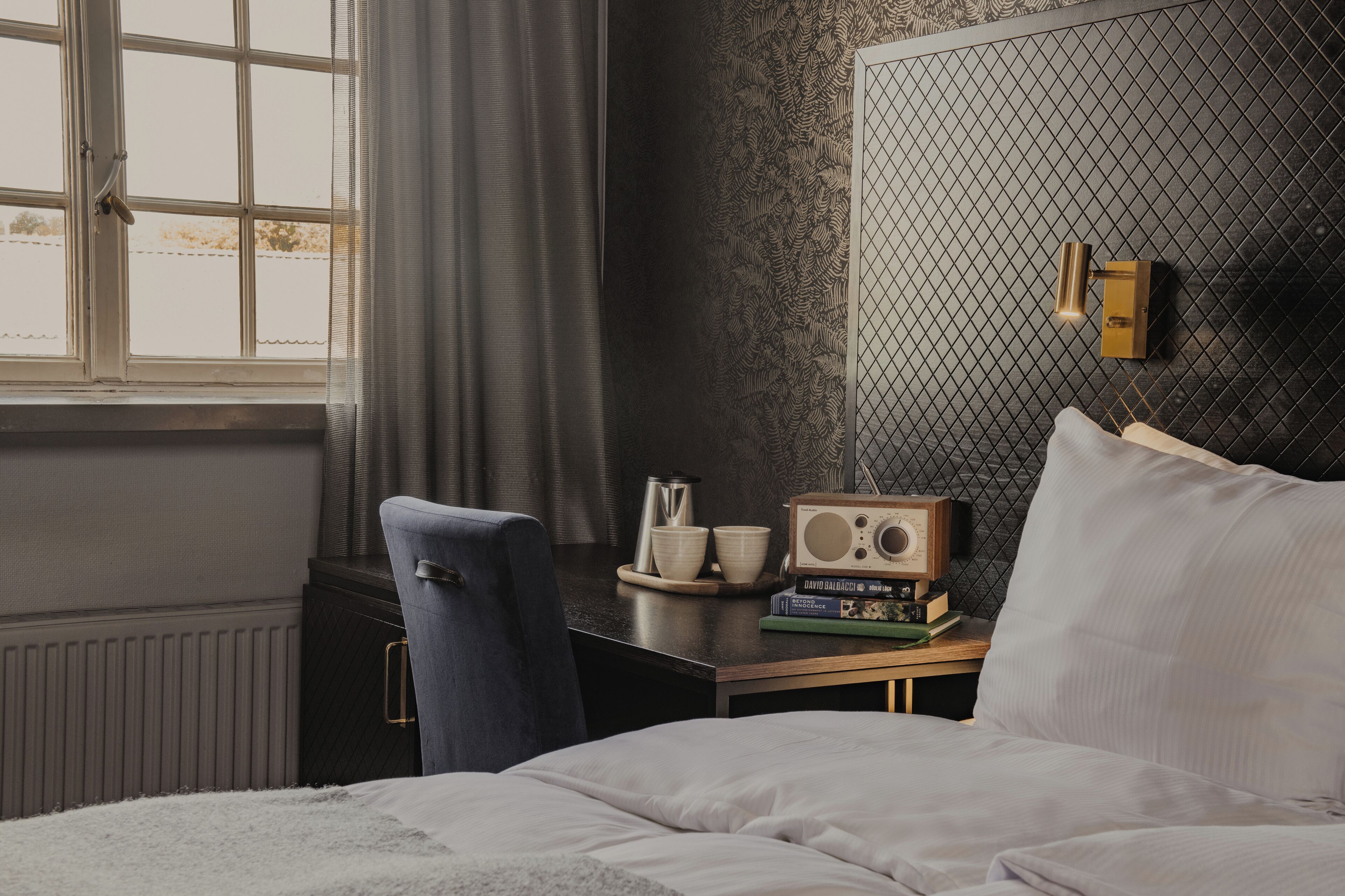 A bedroom with a bed, a desk with a radio, books, and a chair.