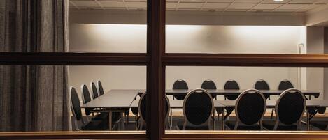 A conference room with a long table and multiple chairs, viewed through a window with wooden frames.