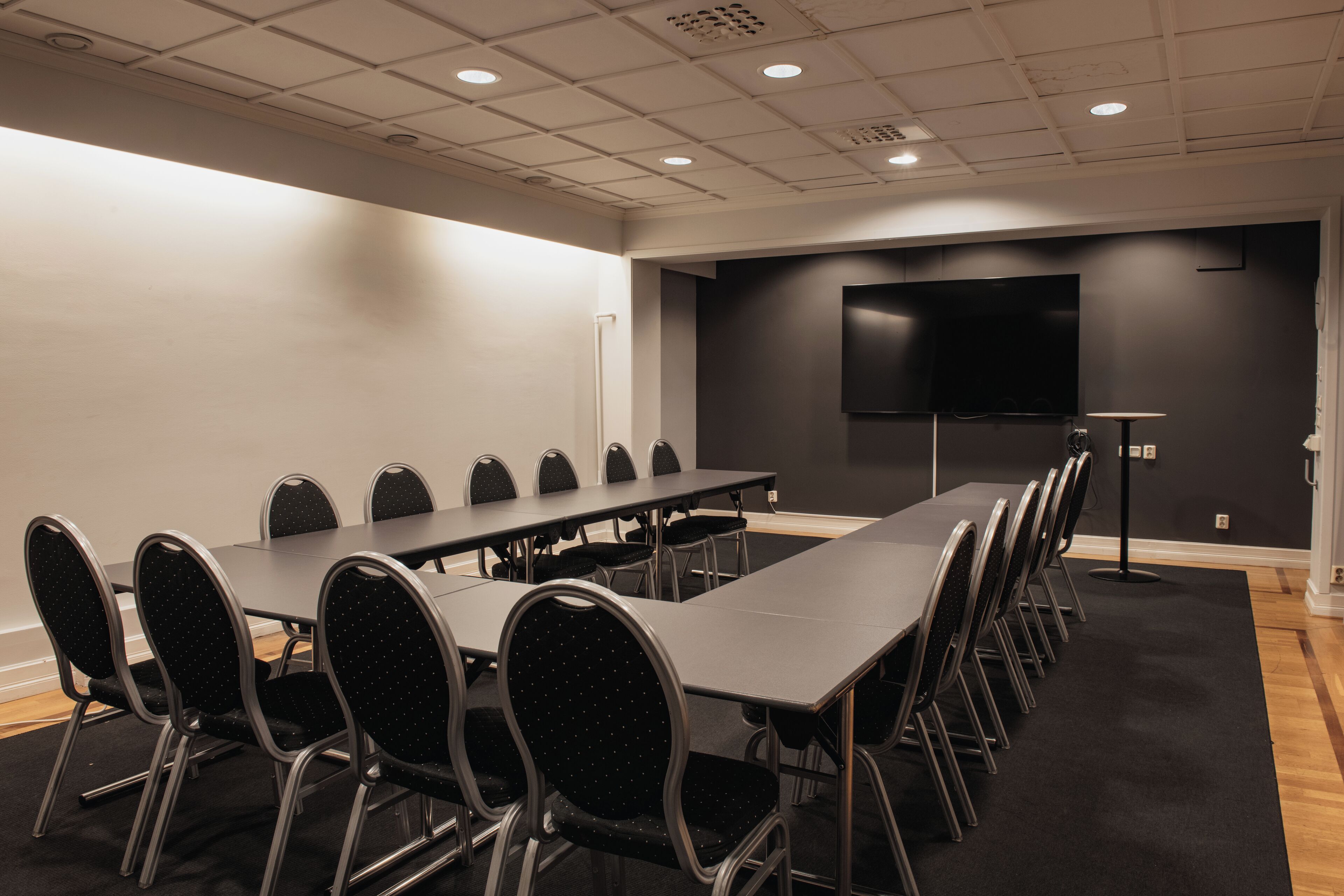 A conference room with a long table, chairs, a projector screen, and a carpeted floor.