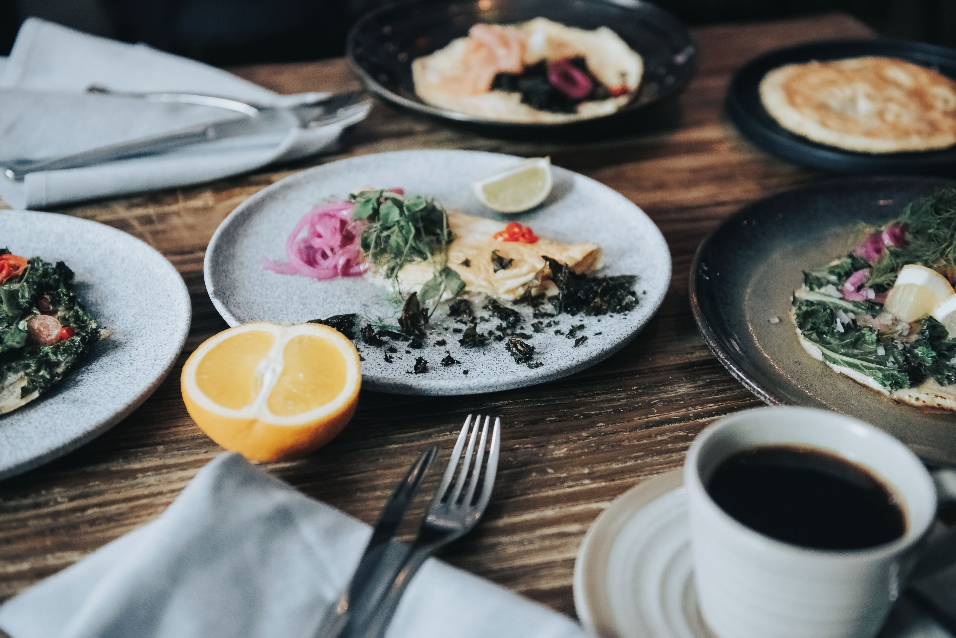 A dining table with plates of food, a cup of coffee, and cutlery.