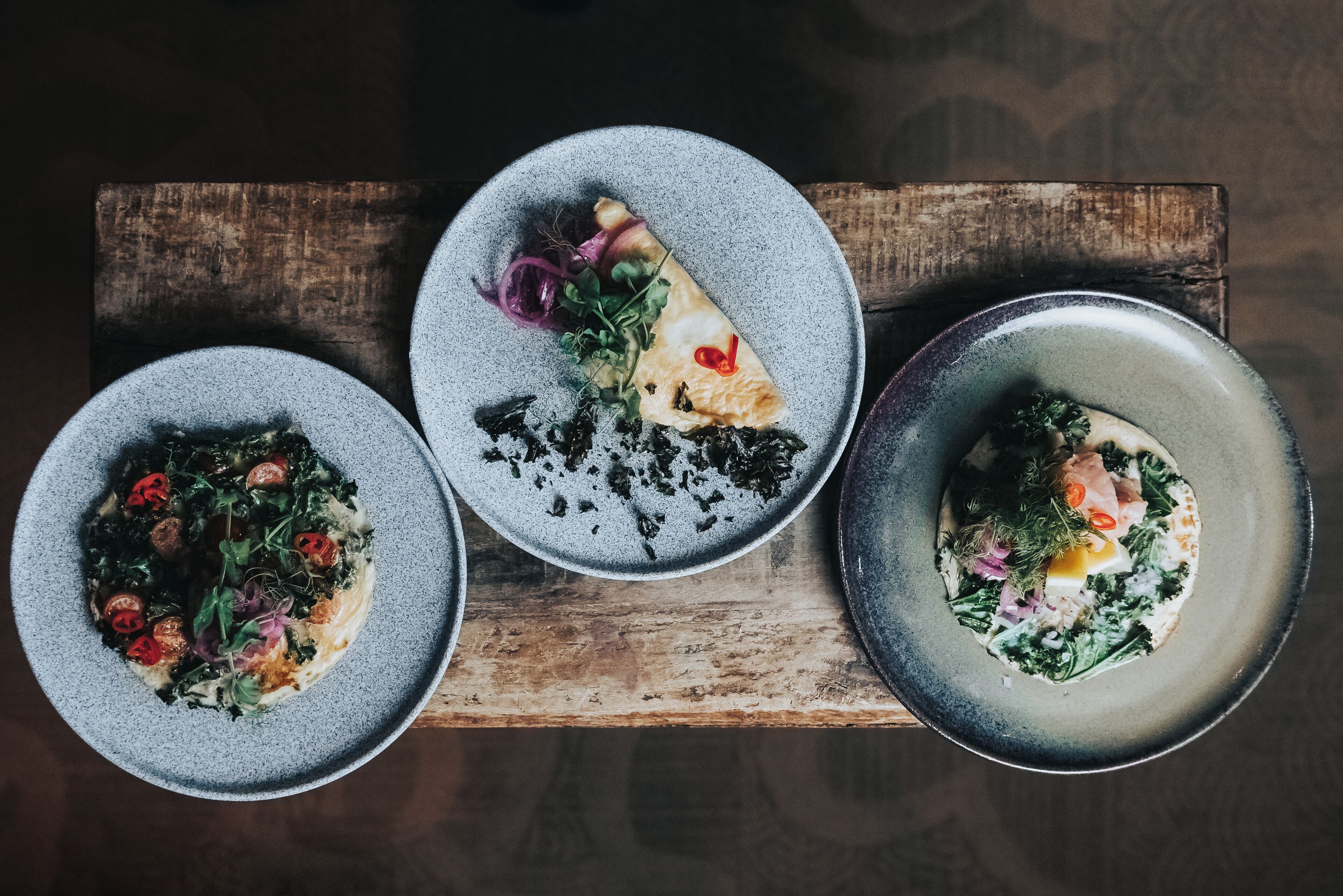 Three plates of food on a wooden board.