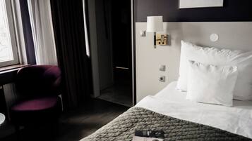 A hotel room with a bed, a chair, a bedside table, and a window with curtains.