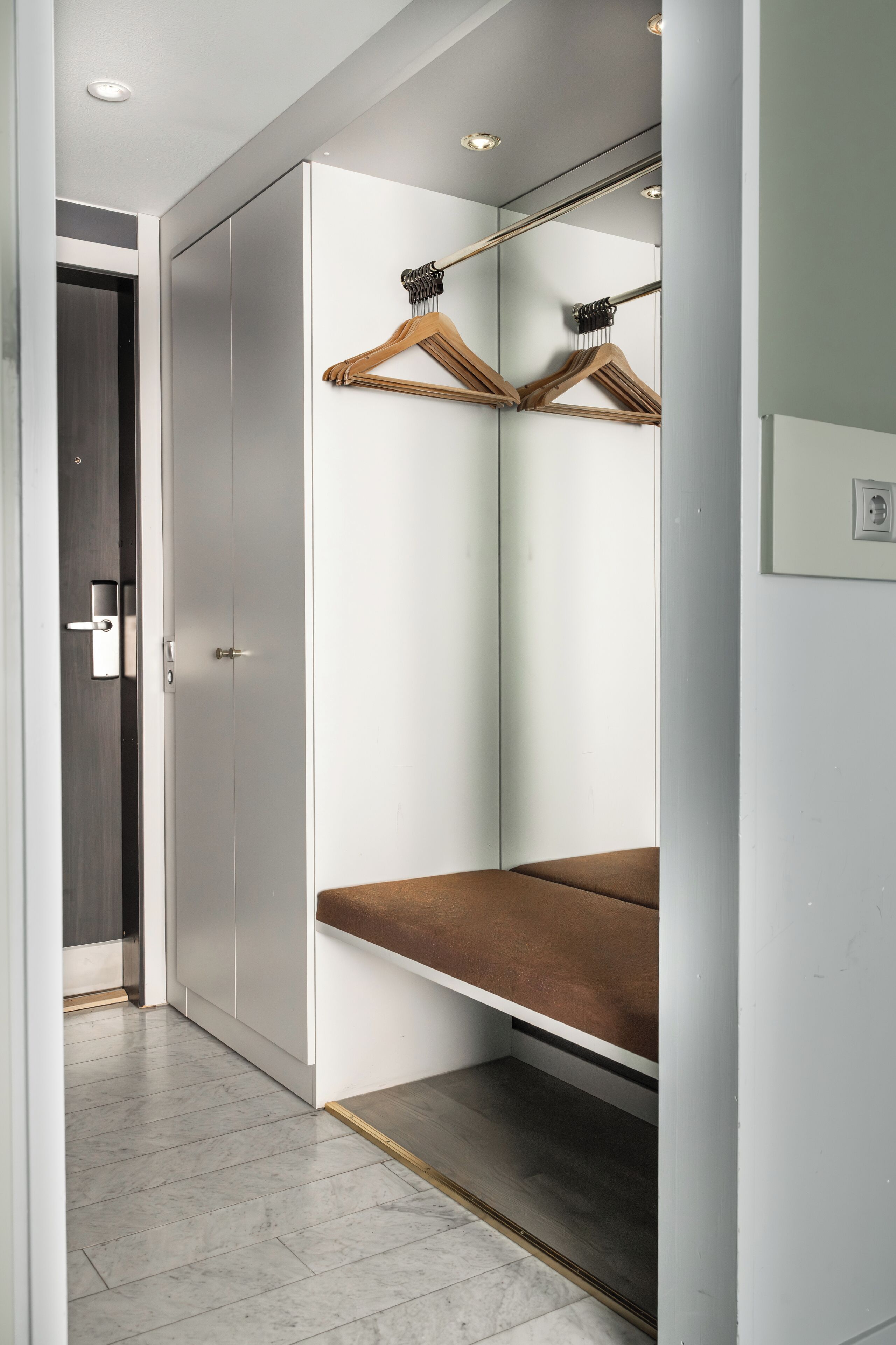 A modern bedroom with a large wardrobe, a mirror, and a bench.