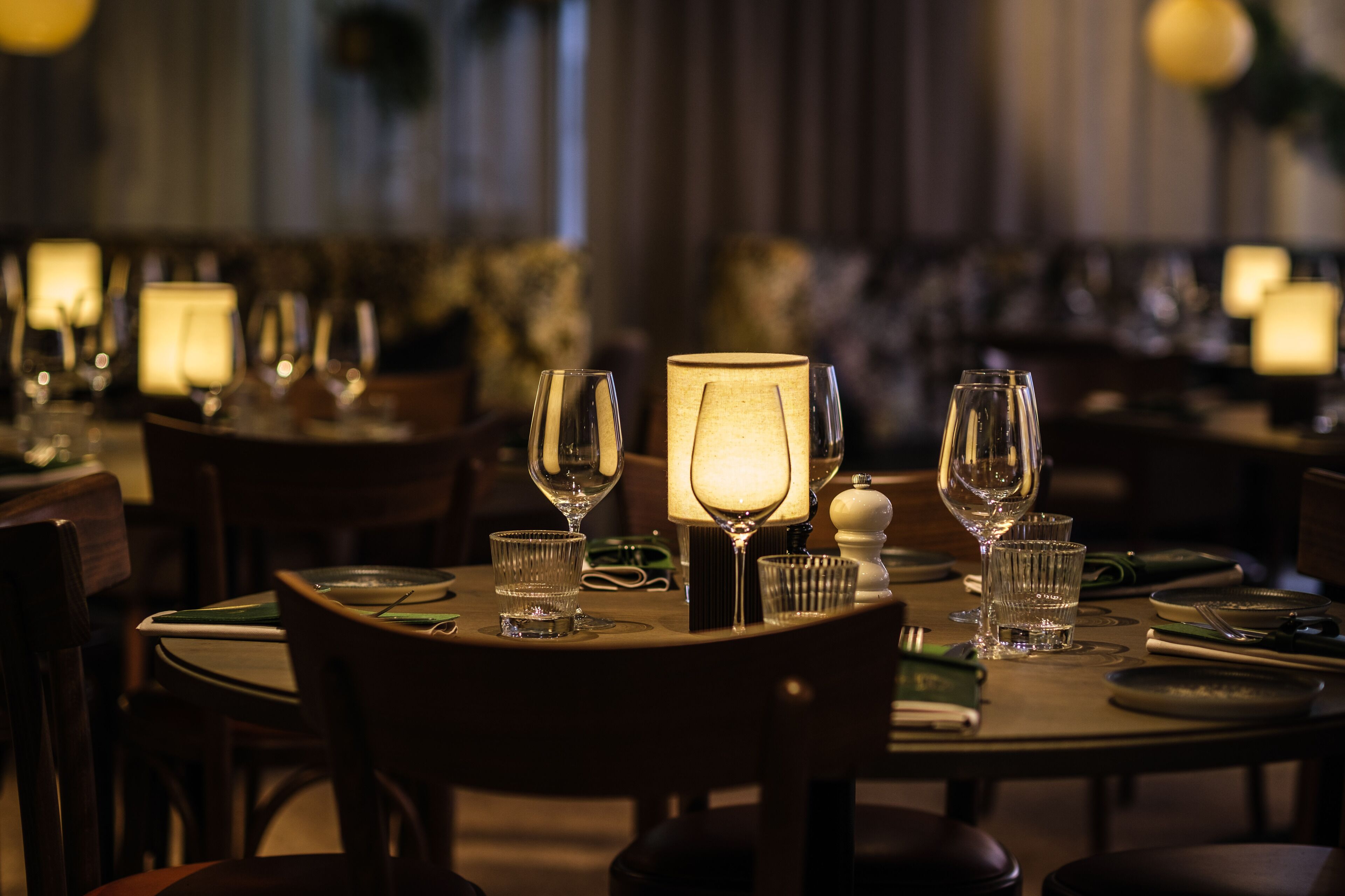 En restaurantindretning i dæmpet belysning med dækketøjet borde, stearinlys og bordlamper.