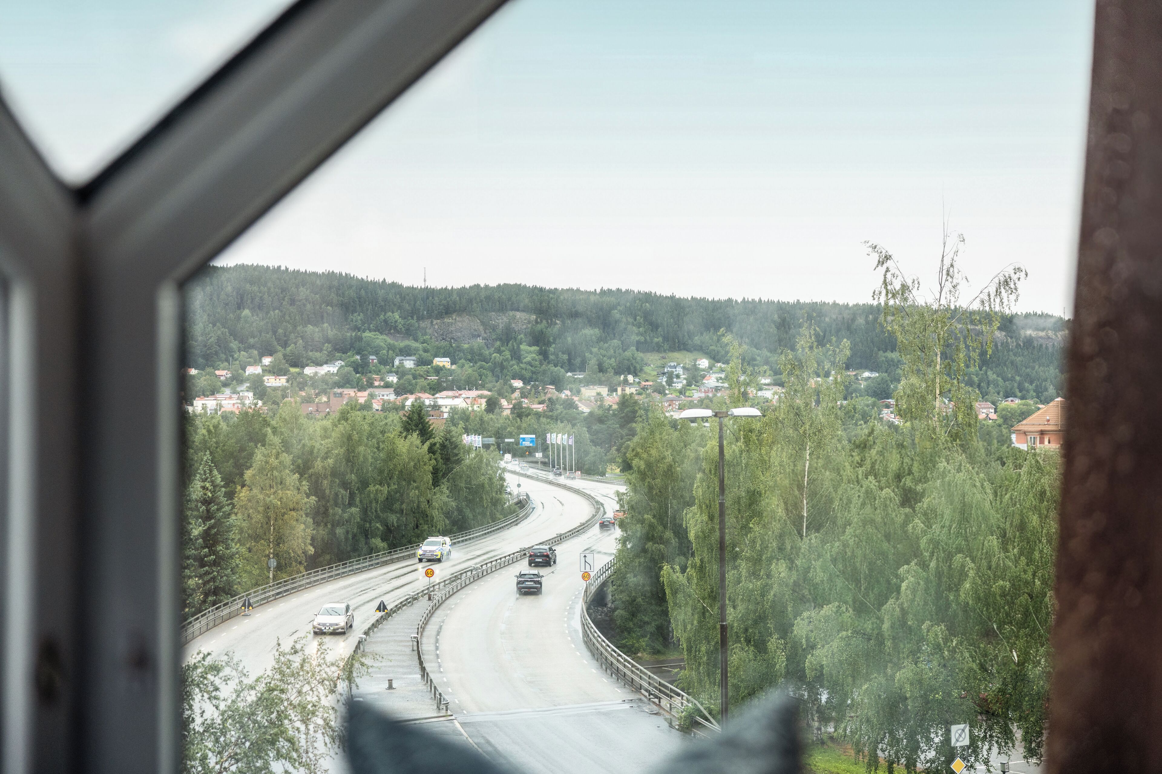 Blick auf eine Autobahn mit mehreren Fahrbahnen und Fahrzeugen, umgeben von Bäumen und Gebäuden in der Ferne.