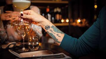 Una persona sosteniendo una copa de cóctel en un bar, con un tatuaje en el brazo.