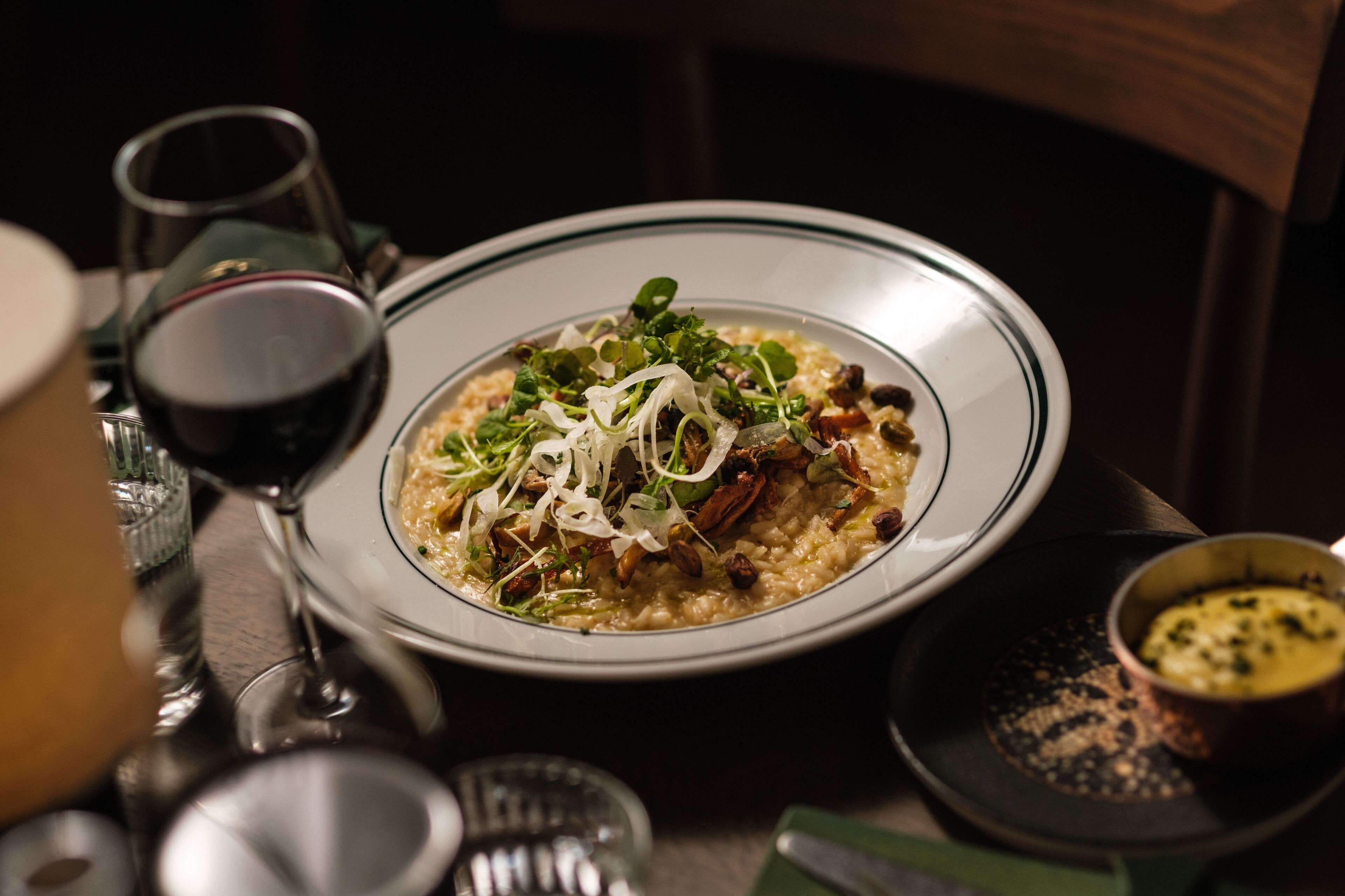 A bowl of food with a glass of red wine and a small bowl of sauce on the table.