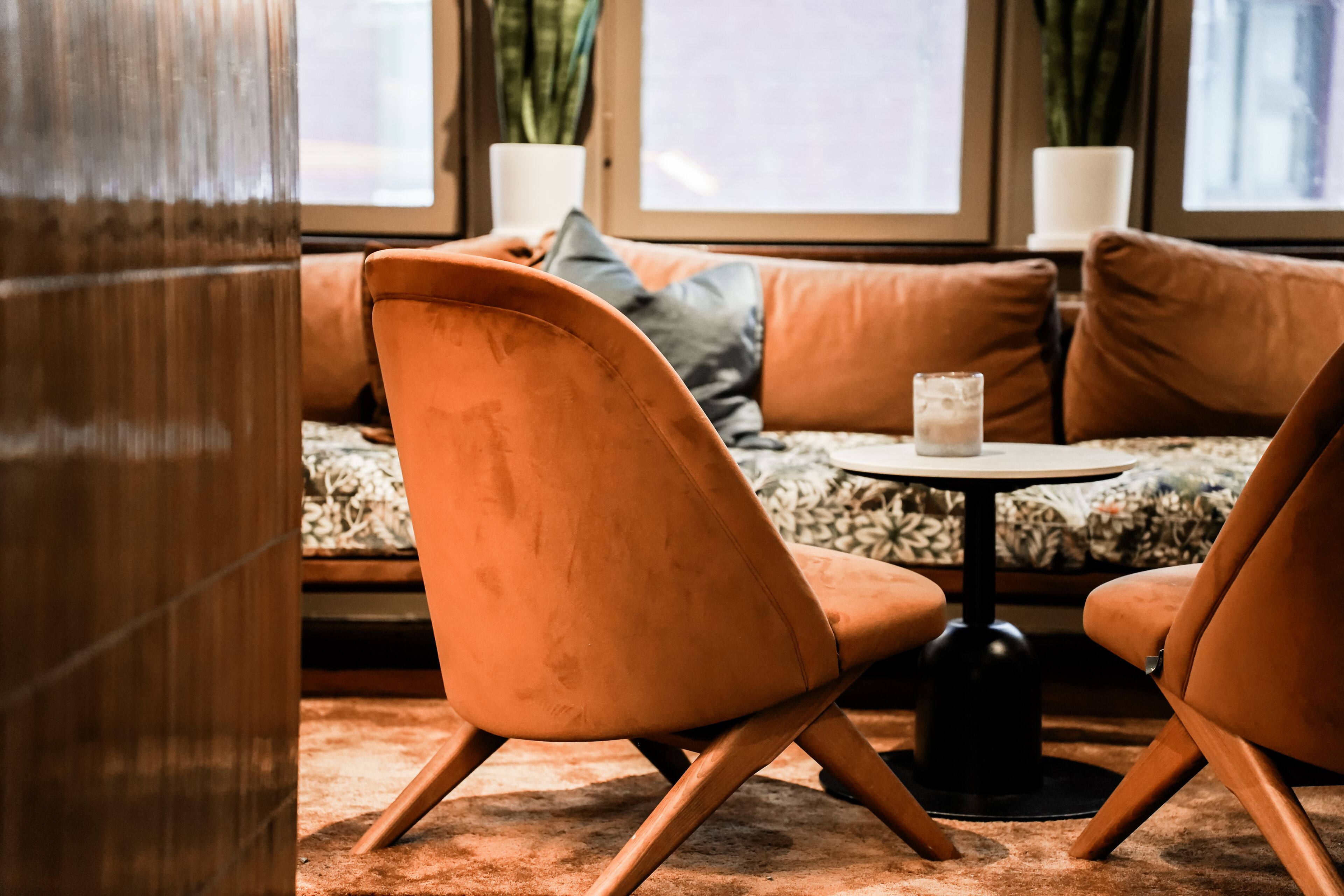 Un rincón acogedor con sofá, dos sillones, una mesita redonda y una ventana con cortinas.