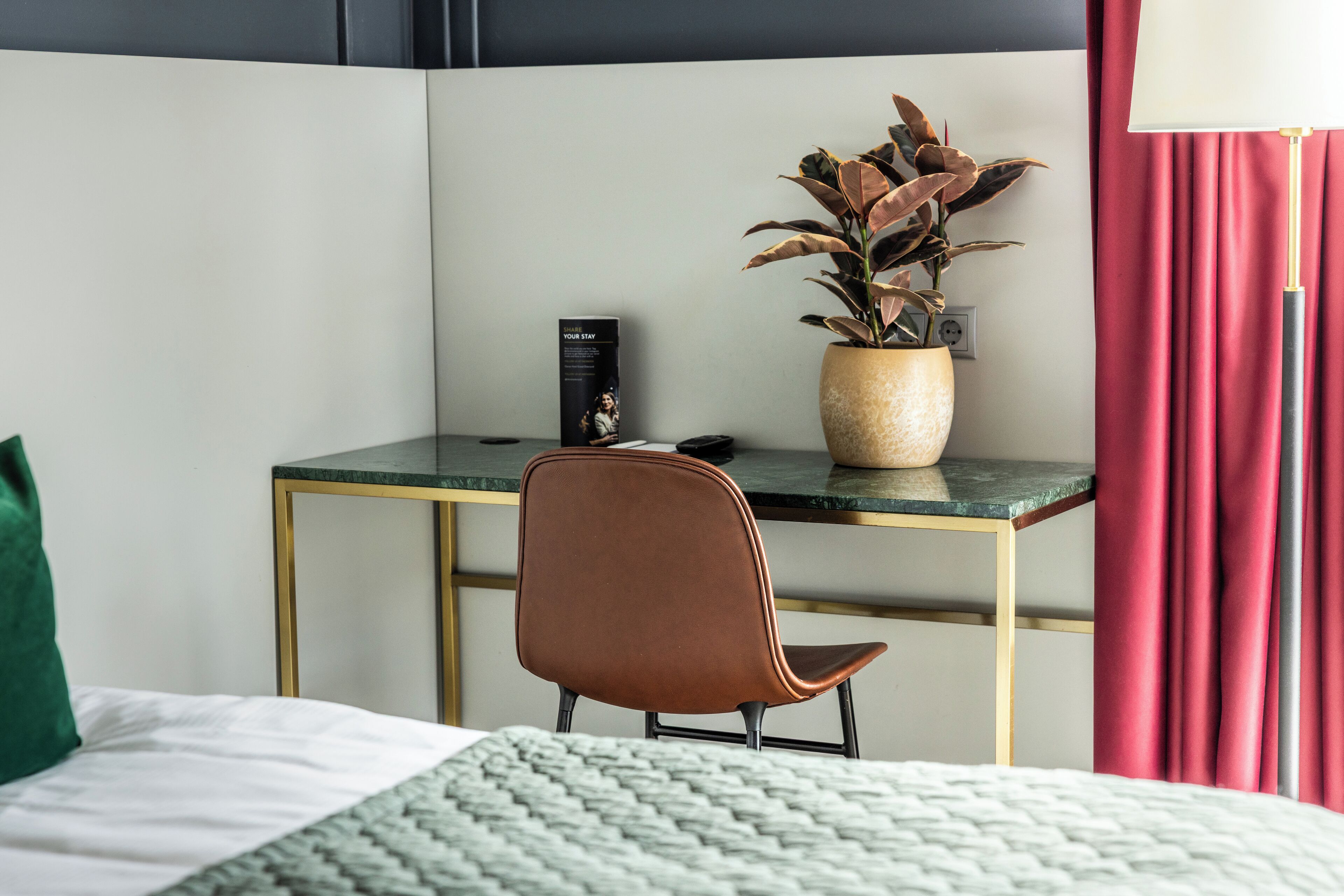 Une chambre d’hôtel avec un lit, un bureau agrémenté d’une plante en pot, une chaise et une lampe.