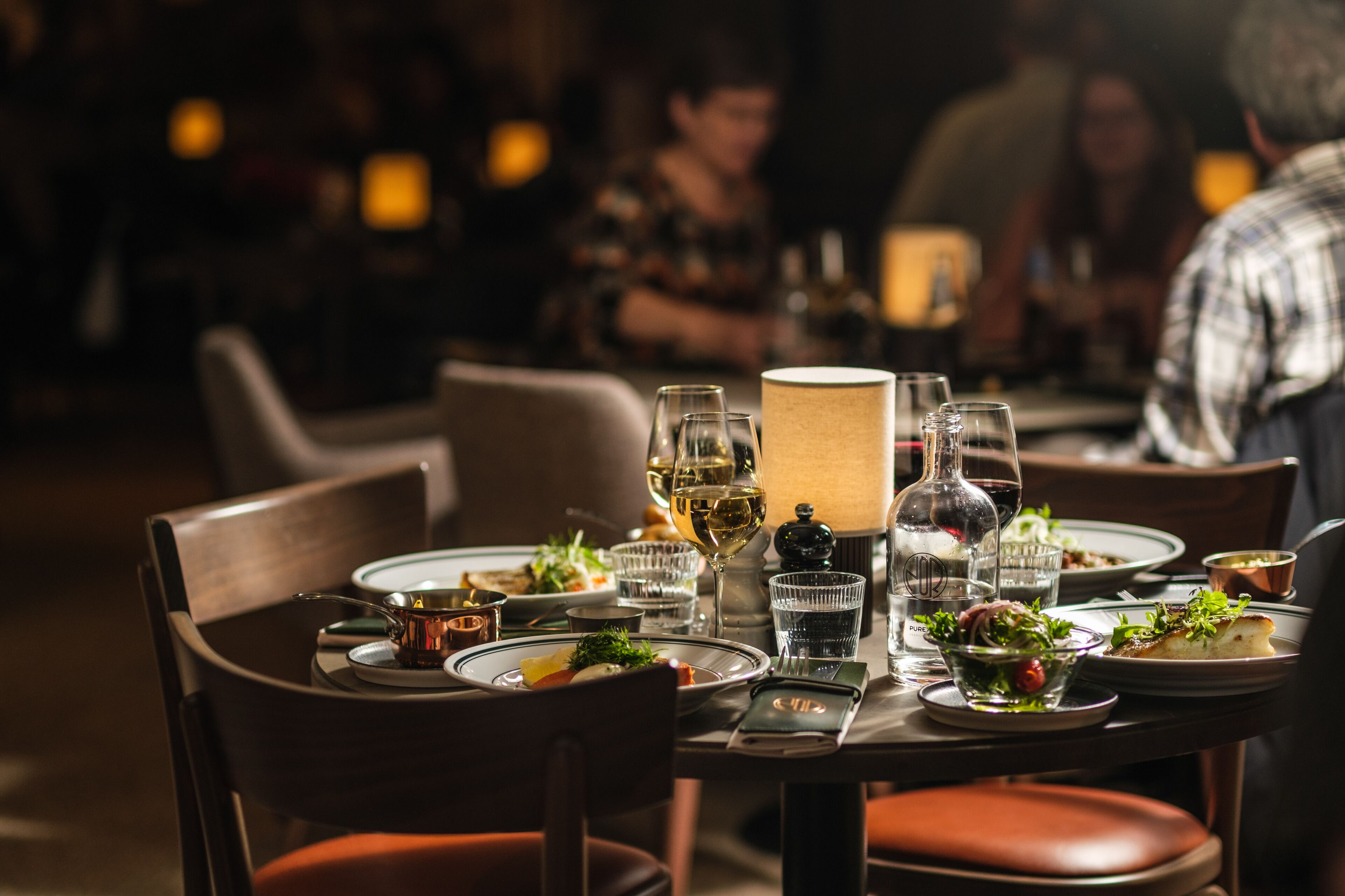 A dining table set with plates, glasses, and a bottle, surrounded by chairs.