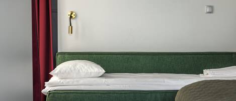 A neatly made bed with white linens and a green headboard, a wall-mounted light fixture, and a door with a golden handle.