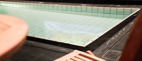 A swimming pool with a tiled floor and a wooden deck area.