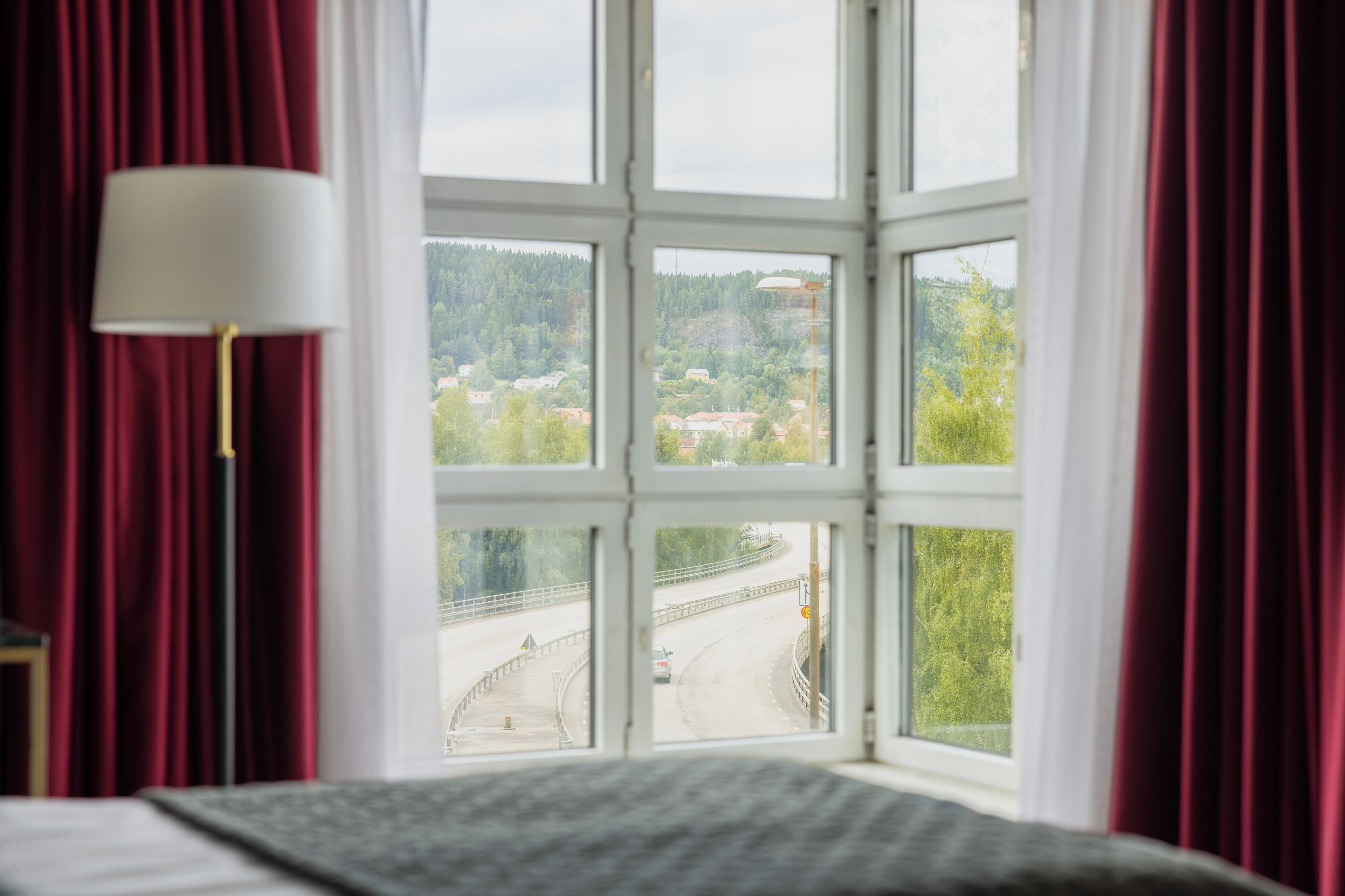 A room with a large window overlooking a road and greenery.
