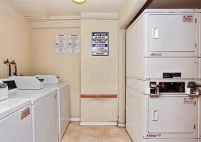 Una sala de lavandería con lavadoras y secadoras apiladas, un letrero informativo y un rótulo de servicios.