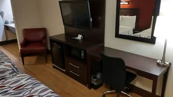 Una habitación de hotel con una cama, un escritorio con televisor, una silla roja y una lámpara de escritorio.