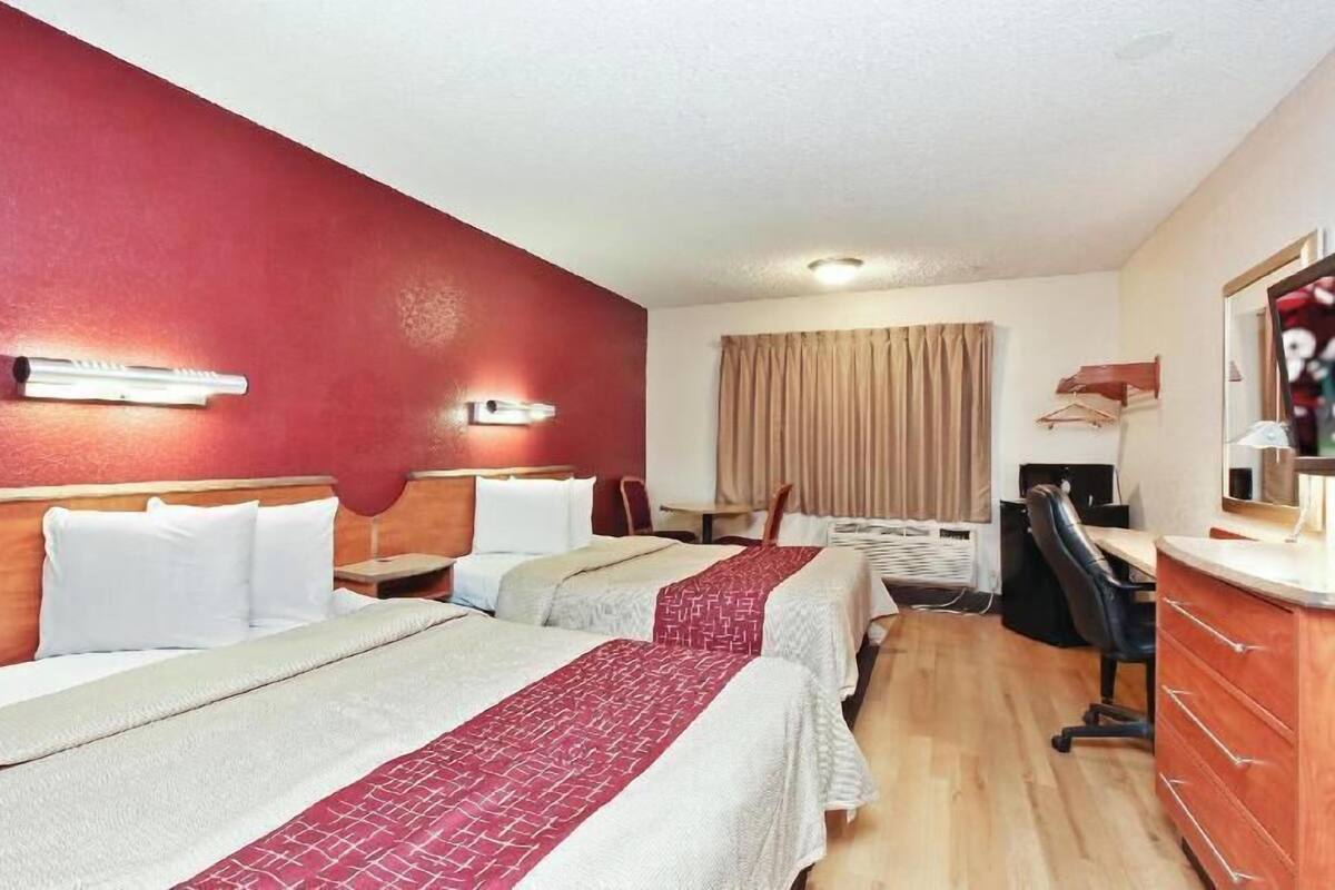 Ein Hotelzimmer mit zwei Betten, einem Schreibtisch, einem Stuhl, einem Fernseher und einem Kleiderschrank.