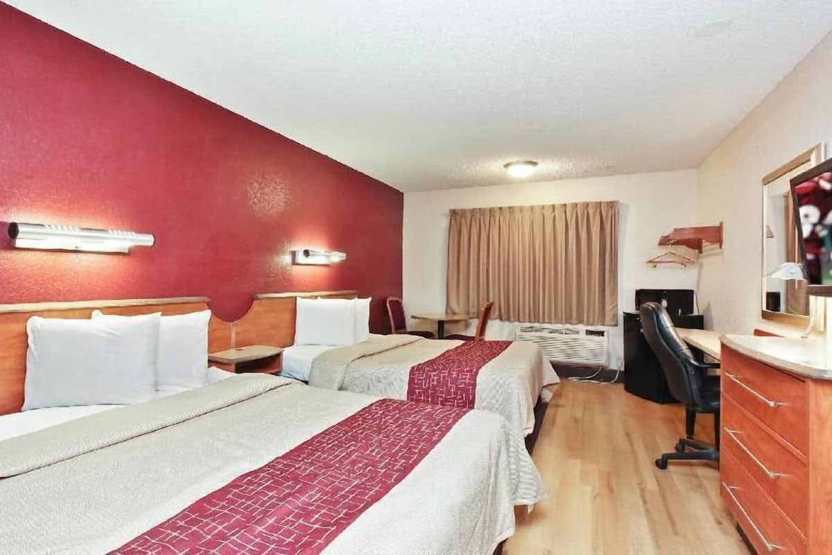 Habitació d'hotel amb dos llits, un escriptori, una cadira, un televisor i un armari.