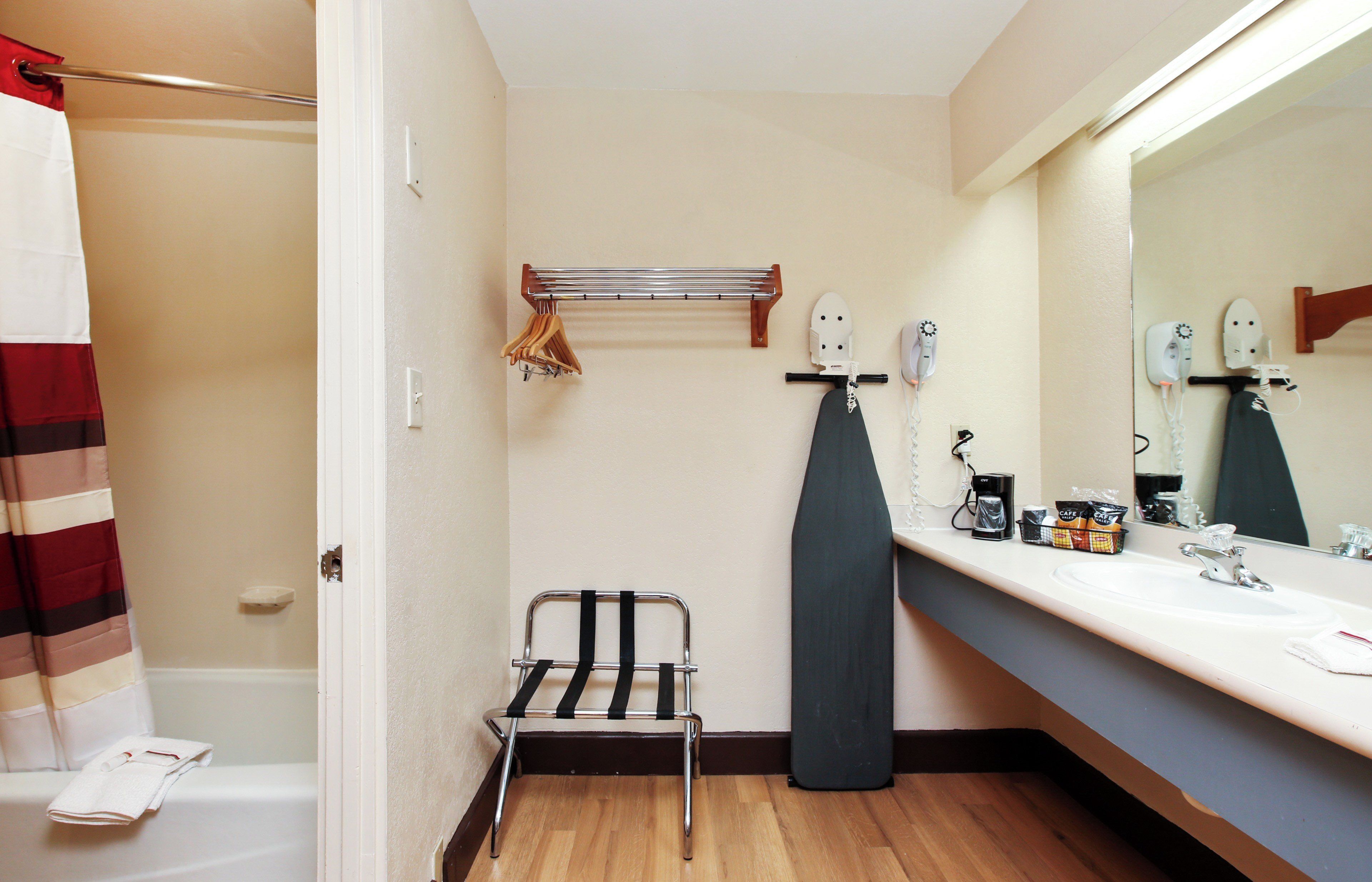 A bathroom with a shower, a towel rack, a hairdryer, a coffee maker, and a mirror.