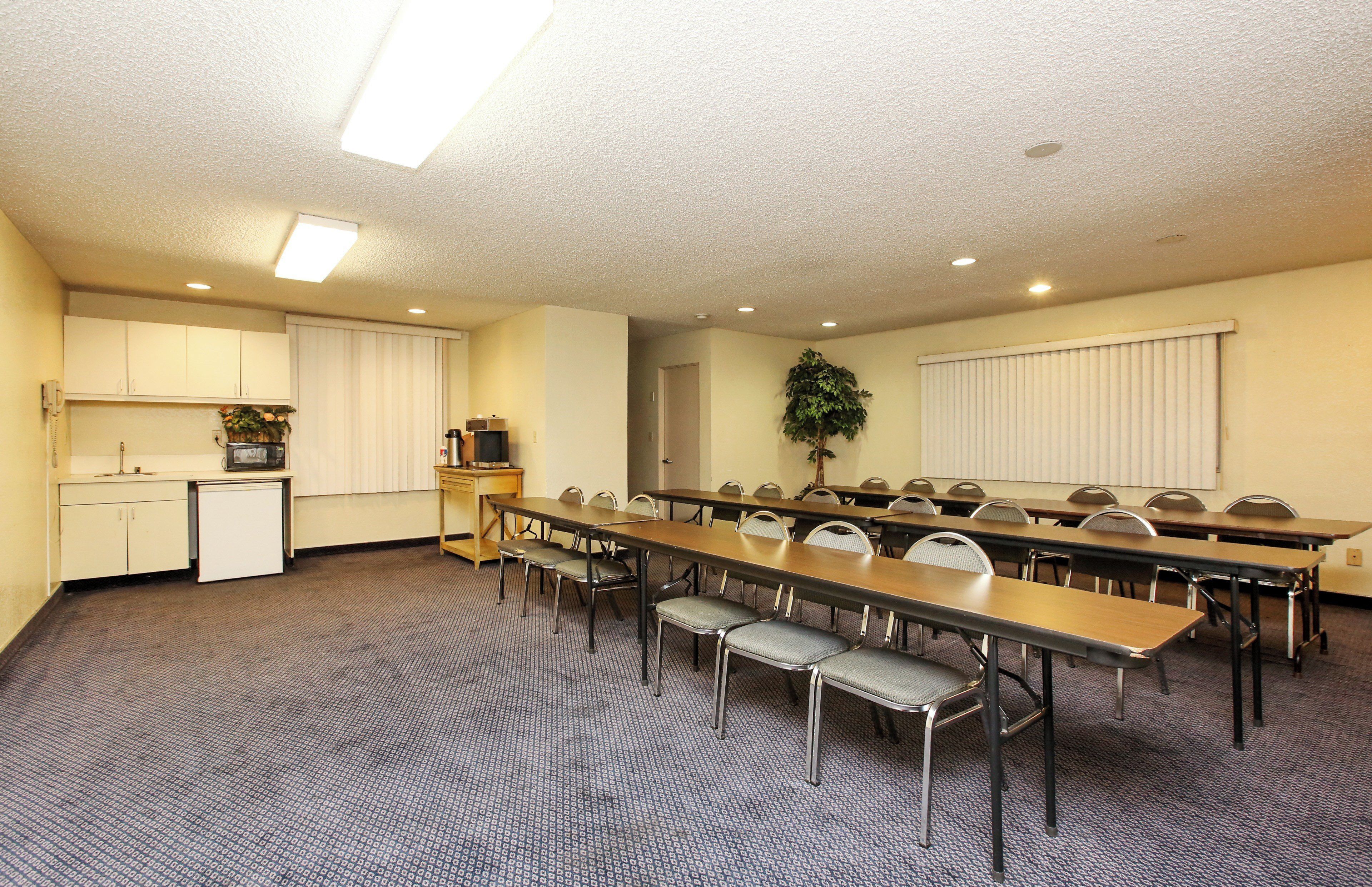 Un salón de conferencias con una mesa larga, sillas, una kitchenette y una planta.