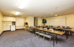 Un salón de conferencias con una mesa larga, sillas, una kitchenette y una planta.