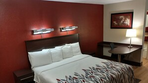 A hotel room with a large bed, a nightstand, a desk, and a chair.