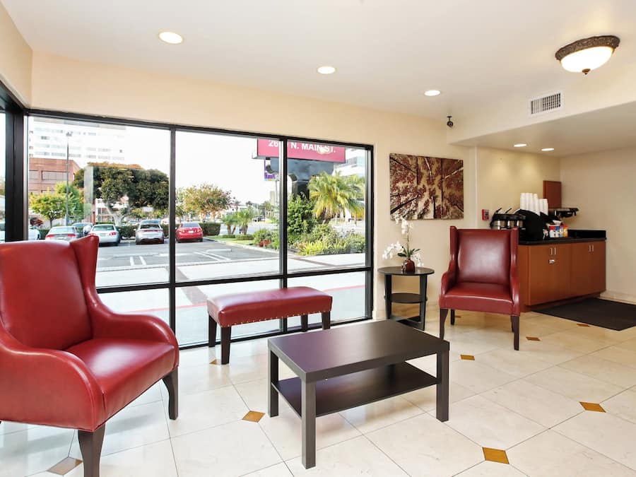 A hotel lobby with a seating area, a reception desk, and a view of the street outside.