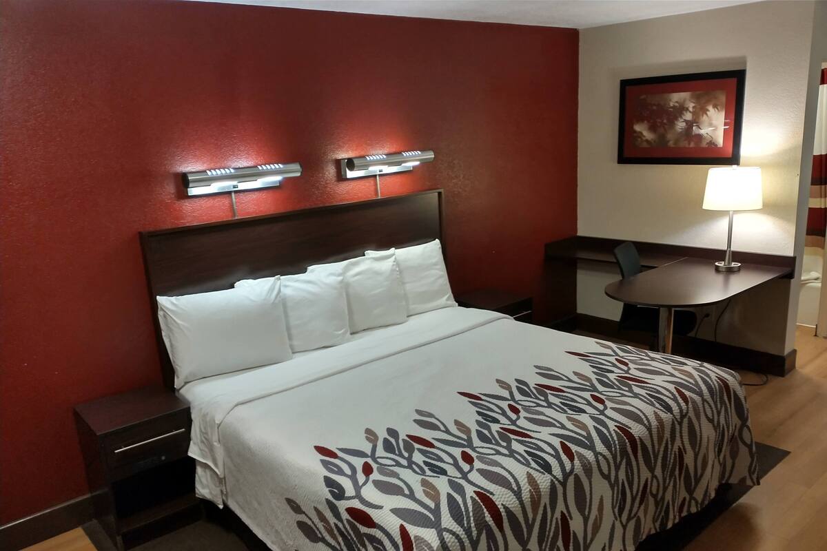 Ein Hotelzimmer mit einem großen Bett, einem Nachttisch, einem Schreibtisch und einem Stuhl.