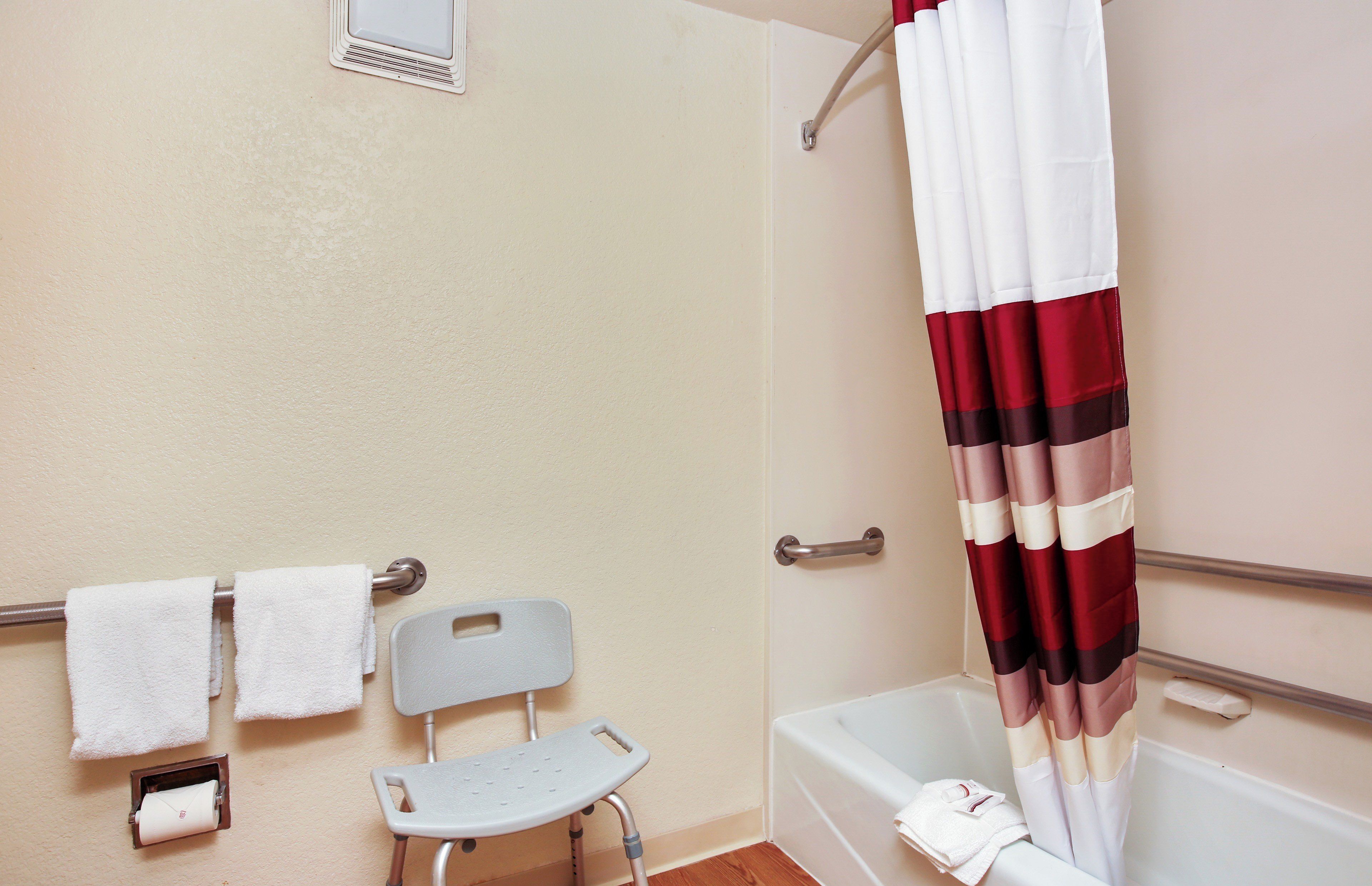 Un baño con ducha, inodoro, barra de apoyo, toallero y un taburete.