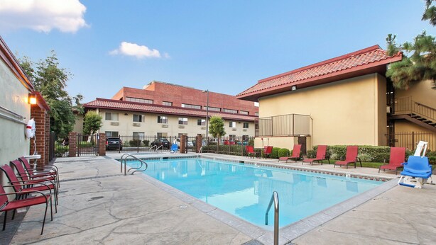 A swimming pool with lounge chairs and a building with a red-tiled roof in the background.