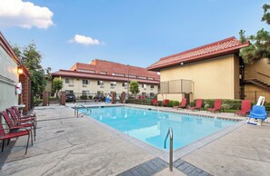 A swimming pool with lounge chairs and a building with a red-tiled roof in the background. - Red Roof Inn Santa Ana (Santa Ana)