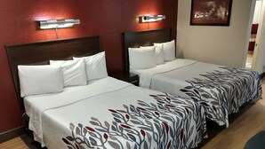 A hotel room with two beds, each with white bedding and a patterned runner. There are wall-mounted lights above each bed, and a framed picture on the wall. - Red Roof Inn Santa Ana (Santa Ana)