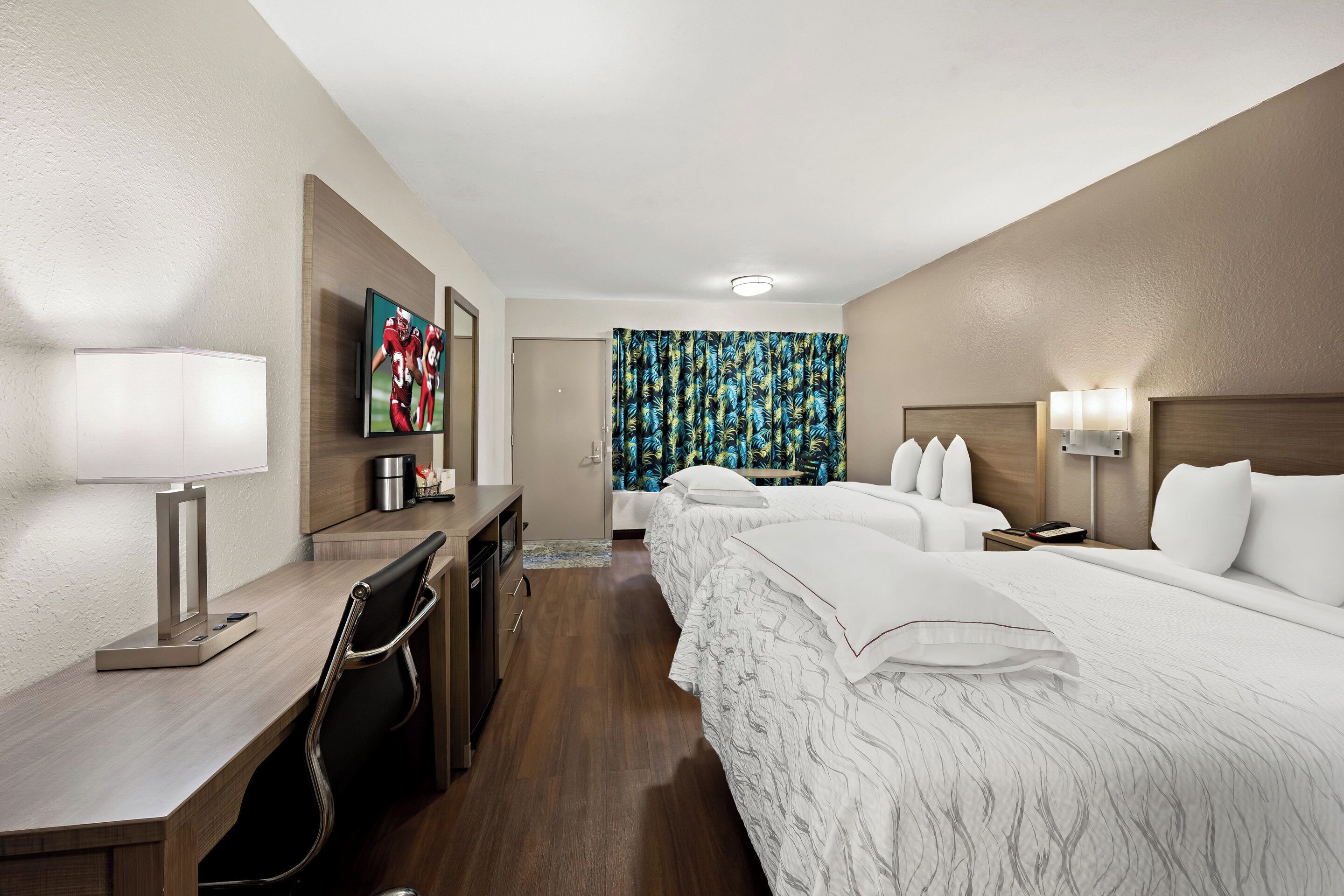 Quarto de hotel com secretária, cama, televisão e banheiro.