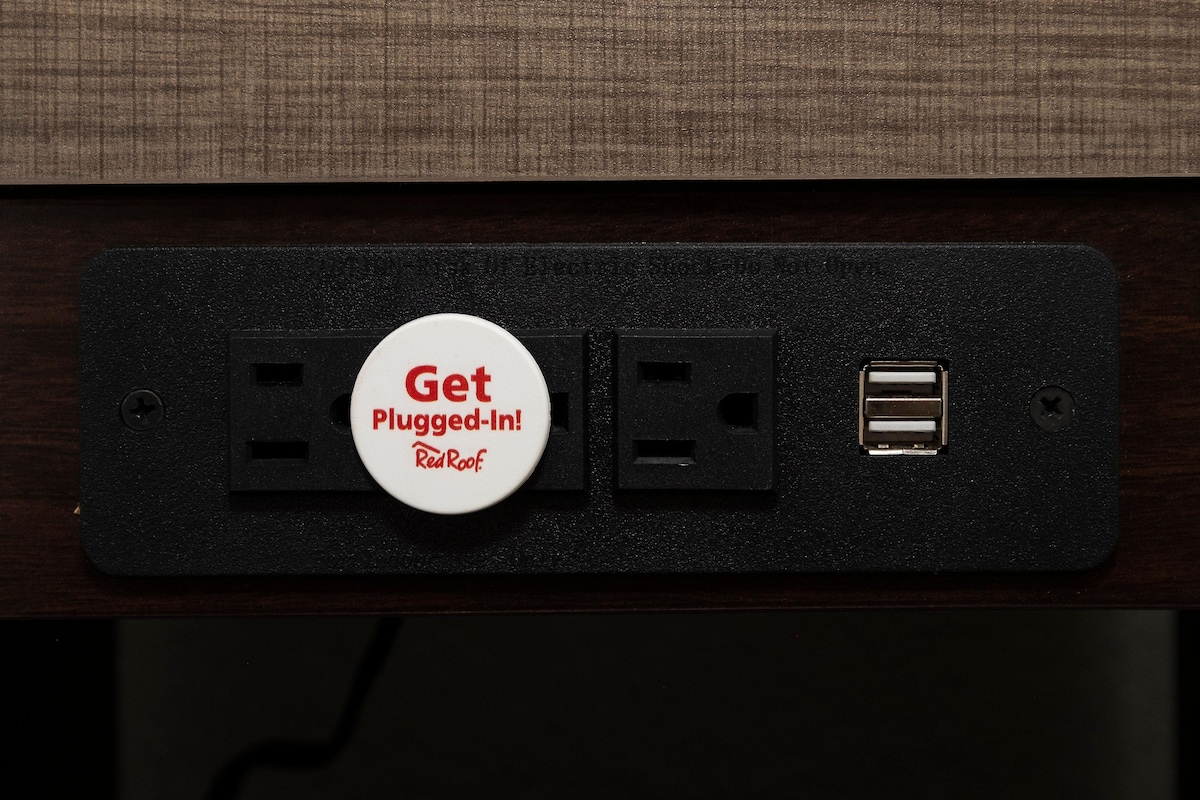 A wall-mounted electrical outlet with a plug-in button labeled "Get Plugged-In! RedRoof."