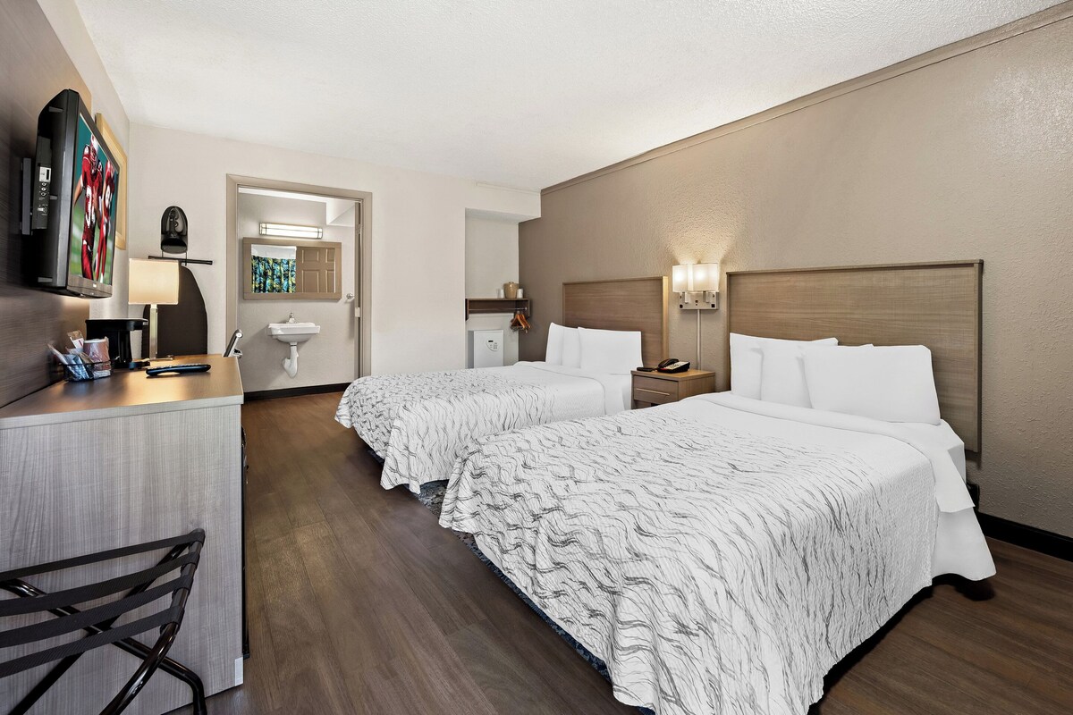 A hotel room with two beds, a desk, a chair, a TV, and a bathroom visible through an open door.