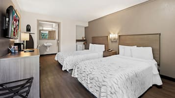 Une chambre d’hôtel avec deux lits, un bureau, une chaise, une télévision et une salle de bain visible à travers une porte ouverte.