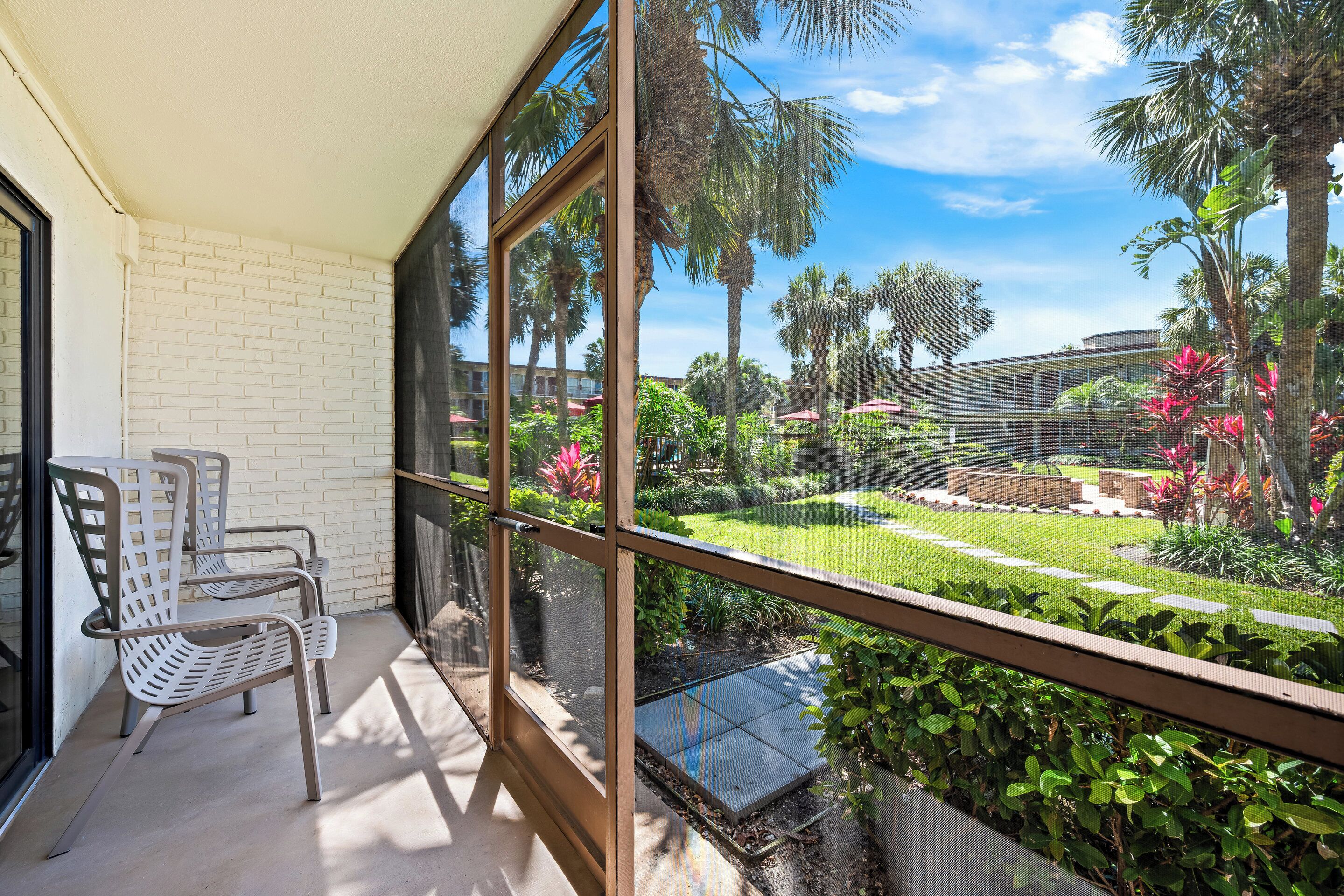 A balcony with a view of a well-maintained garden, including palm trees and various plants.
