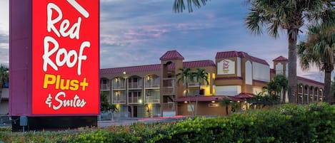 Un hotel llamado Red Roof Plus Suites con un letrero grande, varios balcones y palmeras.