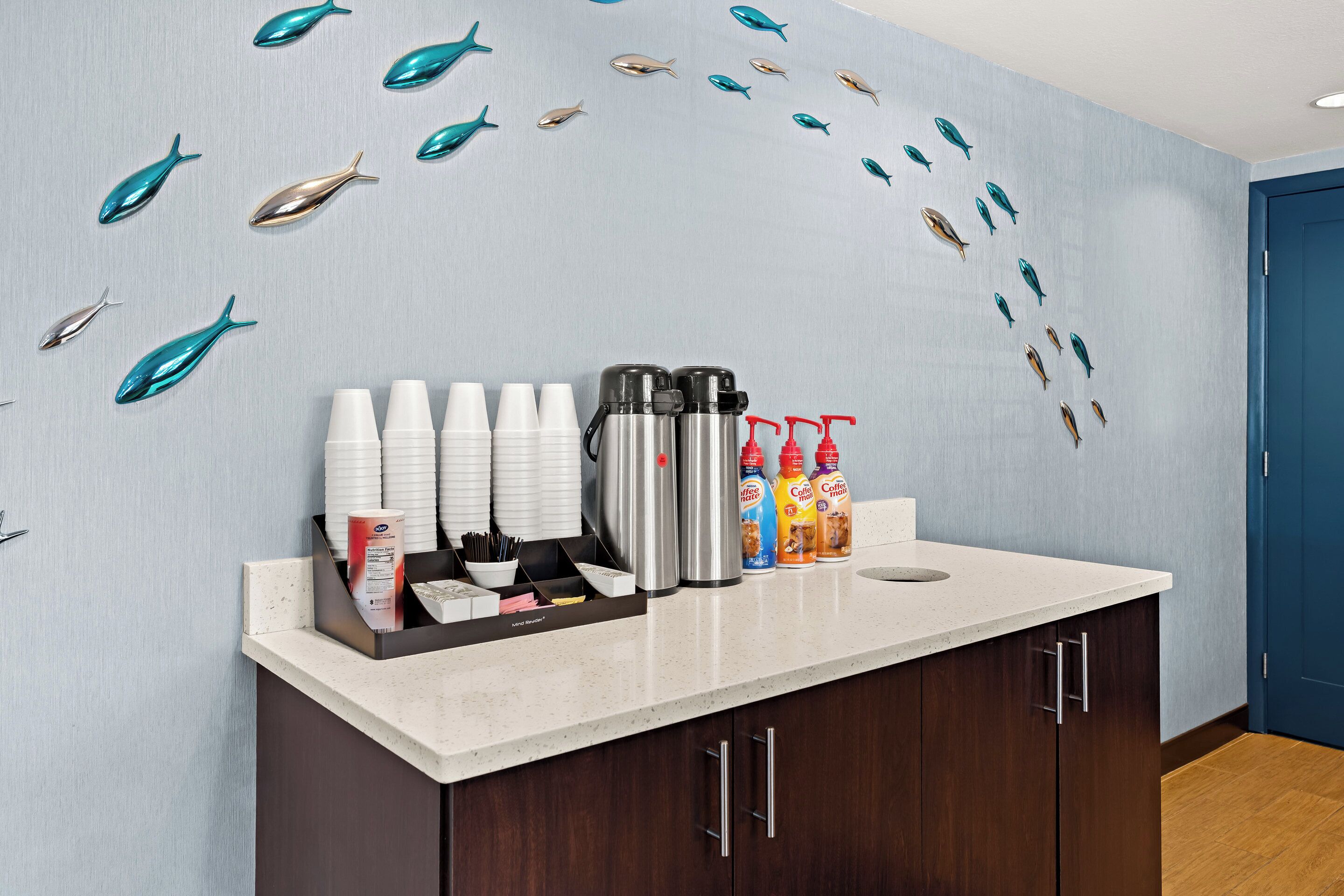 Ein Hotel-Empfangsbereich mit einer Rezeption, die Kaffeetassen, Thermoskannen und Getränkespender präsentiert.