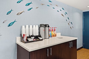 Zona de recepción de un hotel, con mostrador que exhibe tazas de café, termos y dispensadores de bebidas.