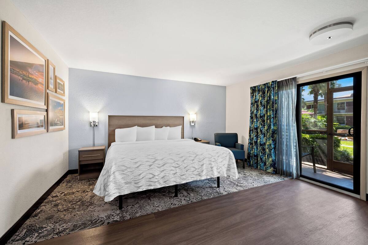 Een hotelkamer met een groot bed, een nachtkastje, een stoel, een raam met gordijnen en lijstwerken aan de muur.